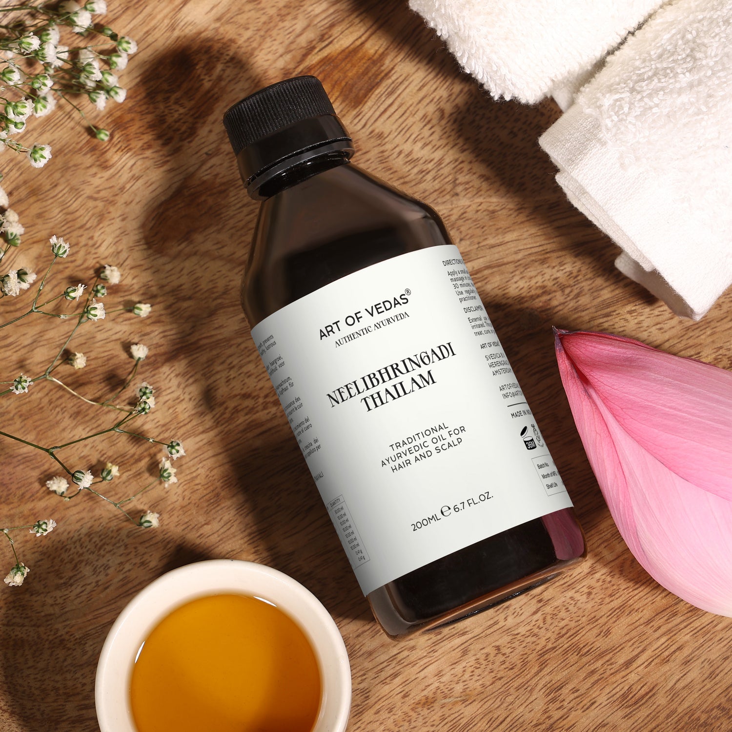Art of Vedas Neelibhringadi Thailam 200ml bottle on wooden surface with oil bowl, flowers, and towel - Ayurvedic Hair Oil for Hair and Scalp
